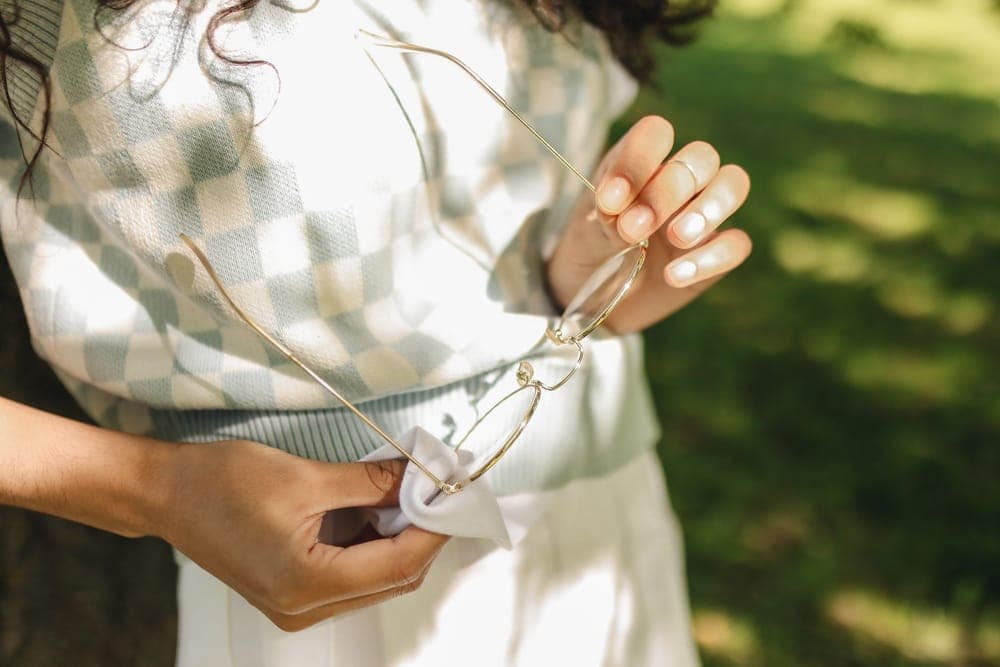 A person wiping a pair of glasses with a cloth outdoors