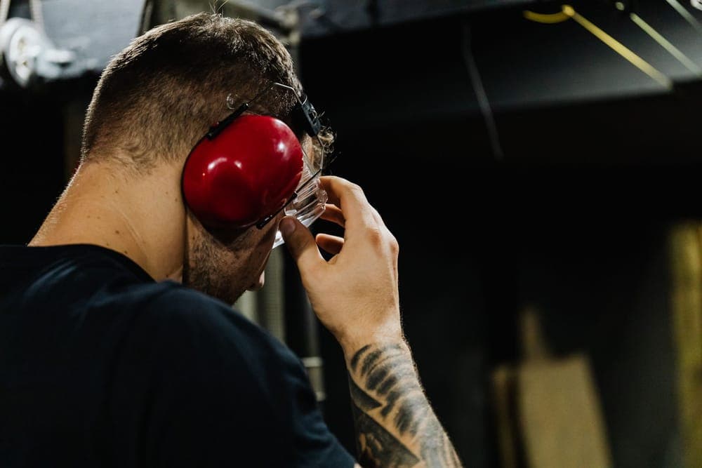 A man adjusting safety glasses while wearing red earmuffs