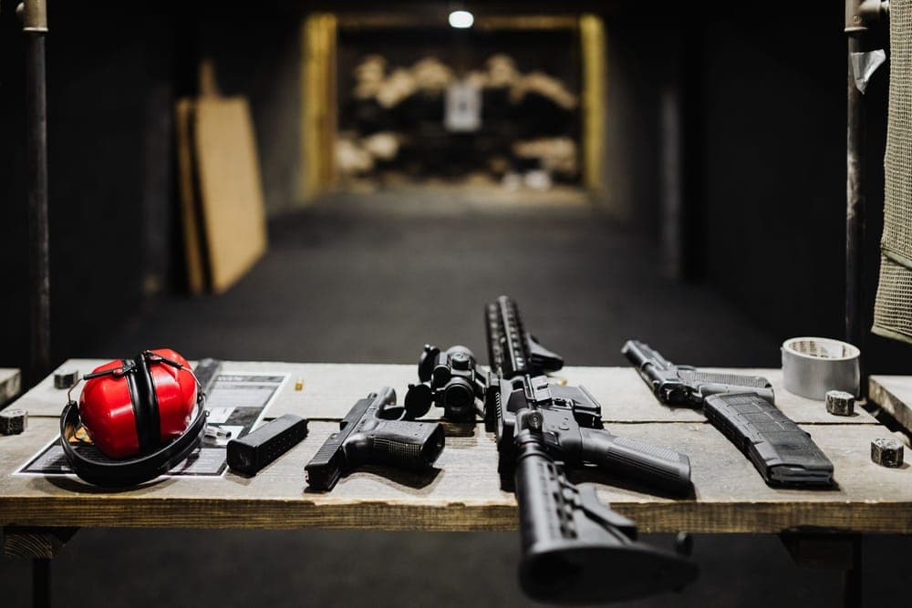 Red earmuffs and firearms laid on a bench at an indoor shooting range