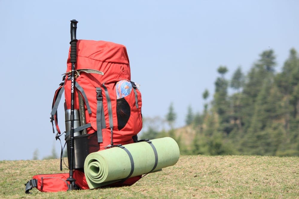 Illustrative stock photo: a red backpack with a sleeping mat standing on a grassy hill