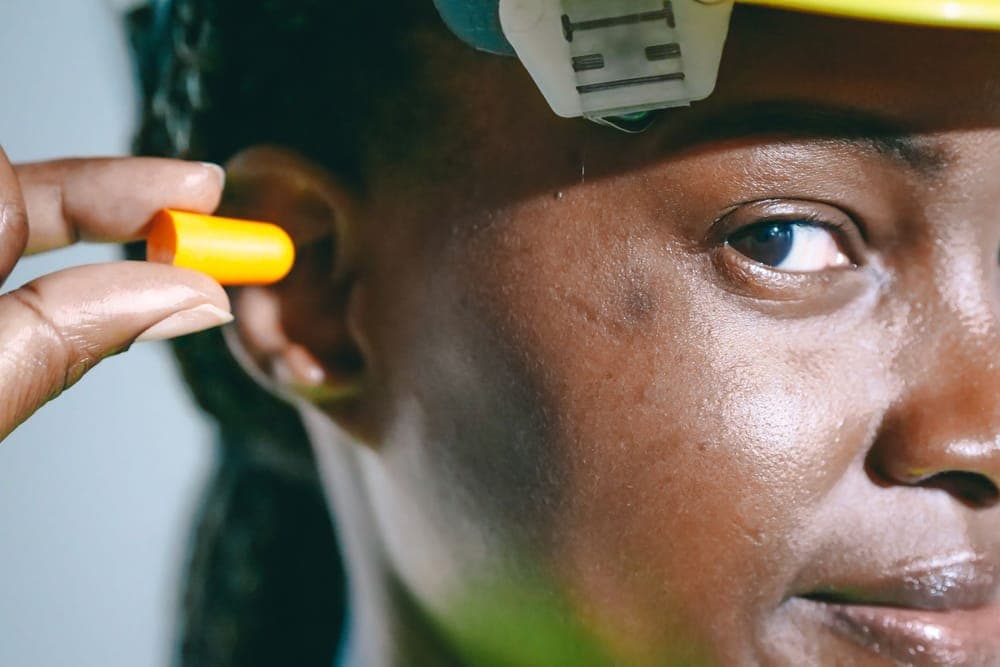 Illustrative stock photo: a woman inserting an orange foam earplug
