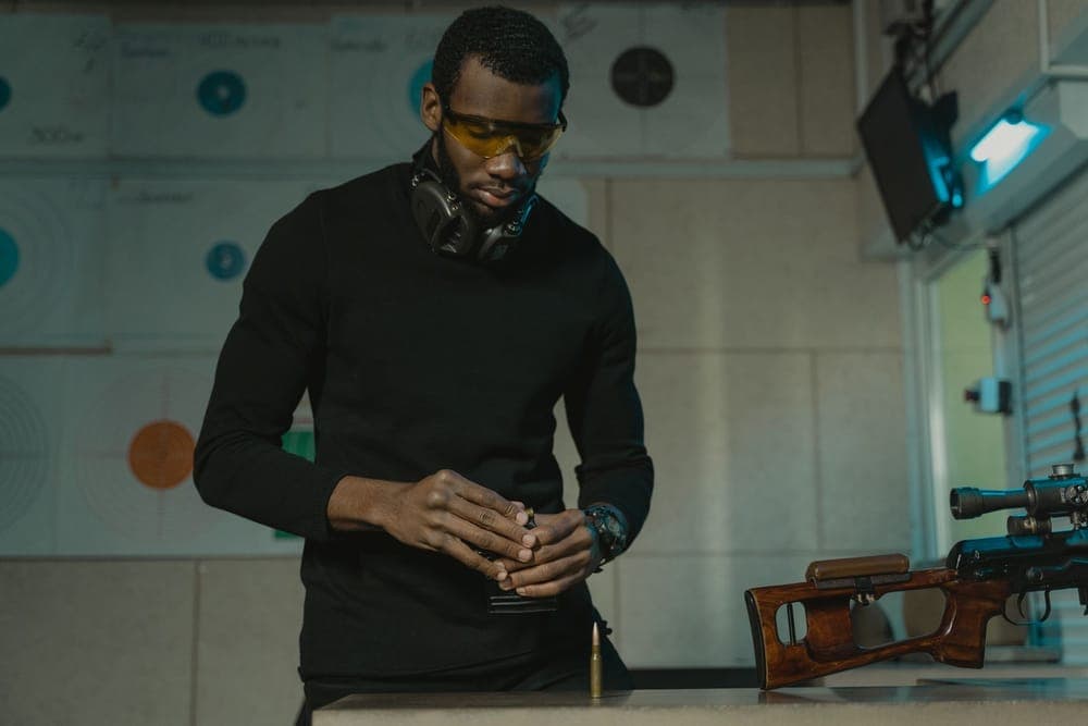 A man in amber safety glasses, with earmuffs around his neck, loading a magazine at a range bench
