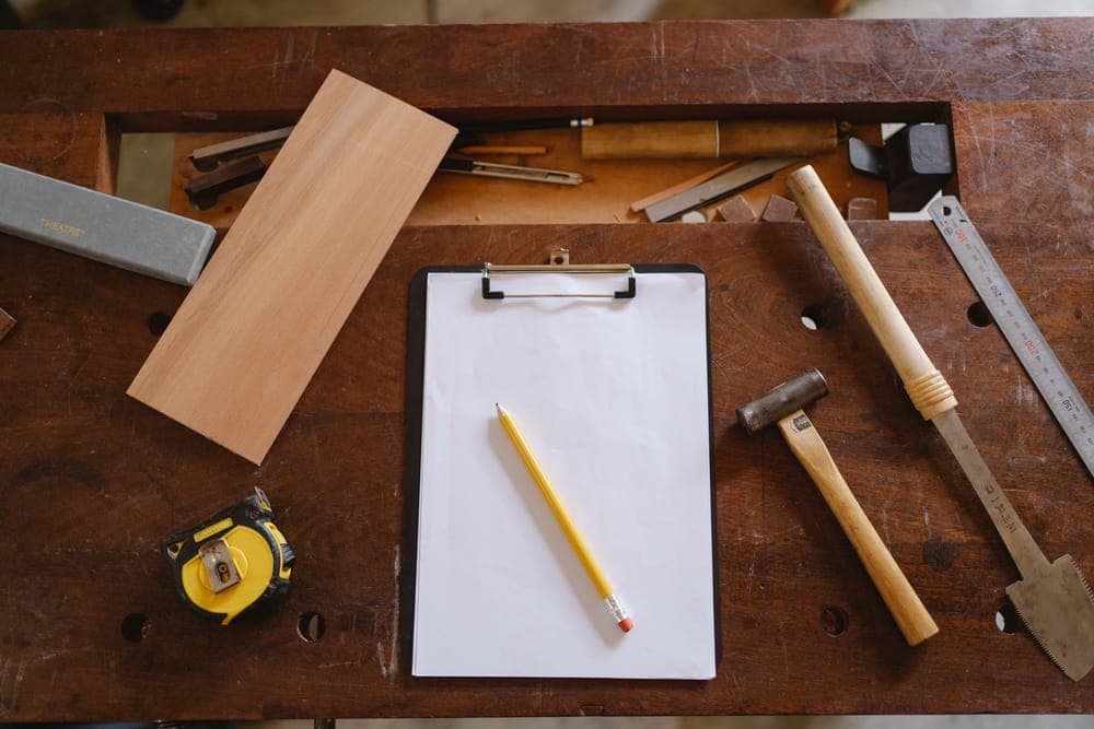 Illustrative stock photo: tools, a tape measure and a clipboard on a wooden workbench