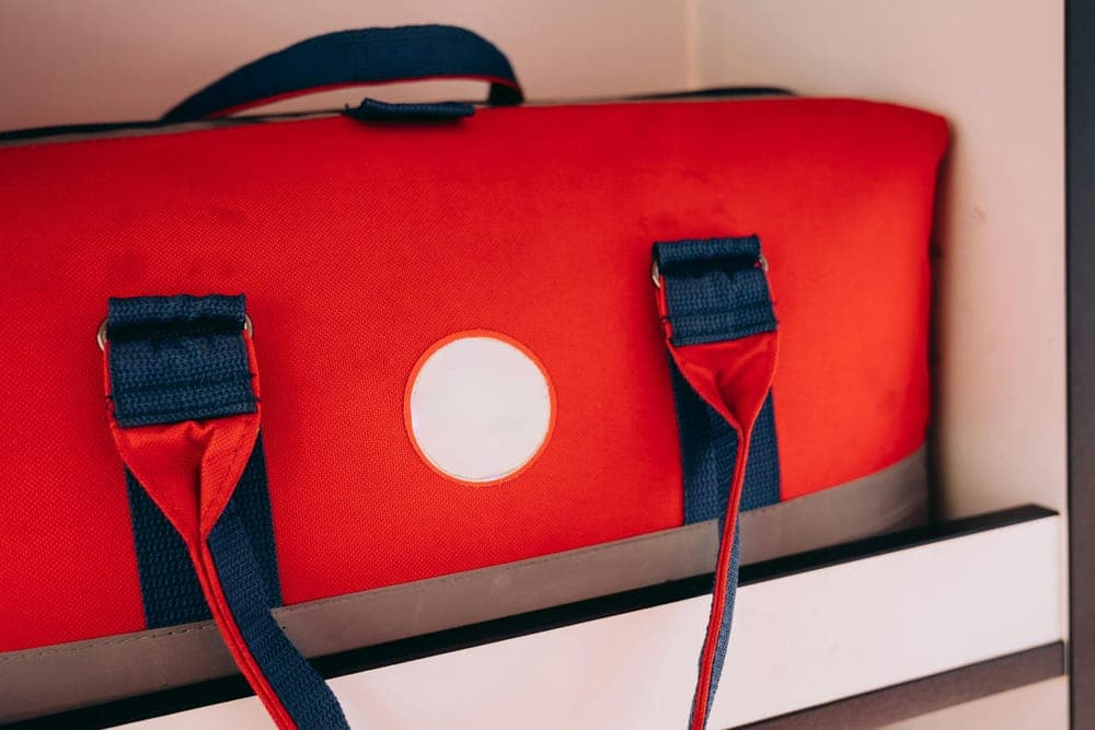 Illustrative stock photo: a red duffel bag with blue straps on a shelf