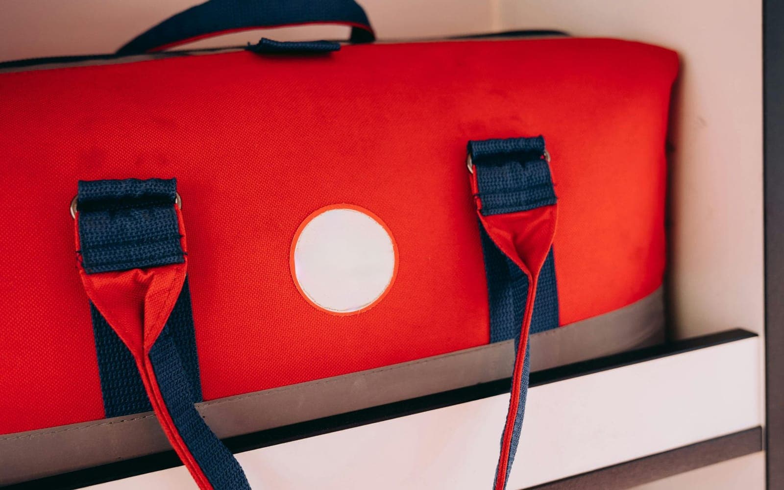 A red duffel bag with blue straps on a shelf
