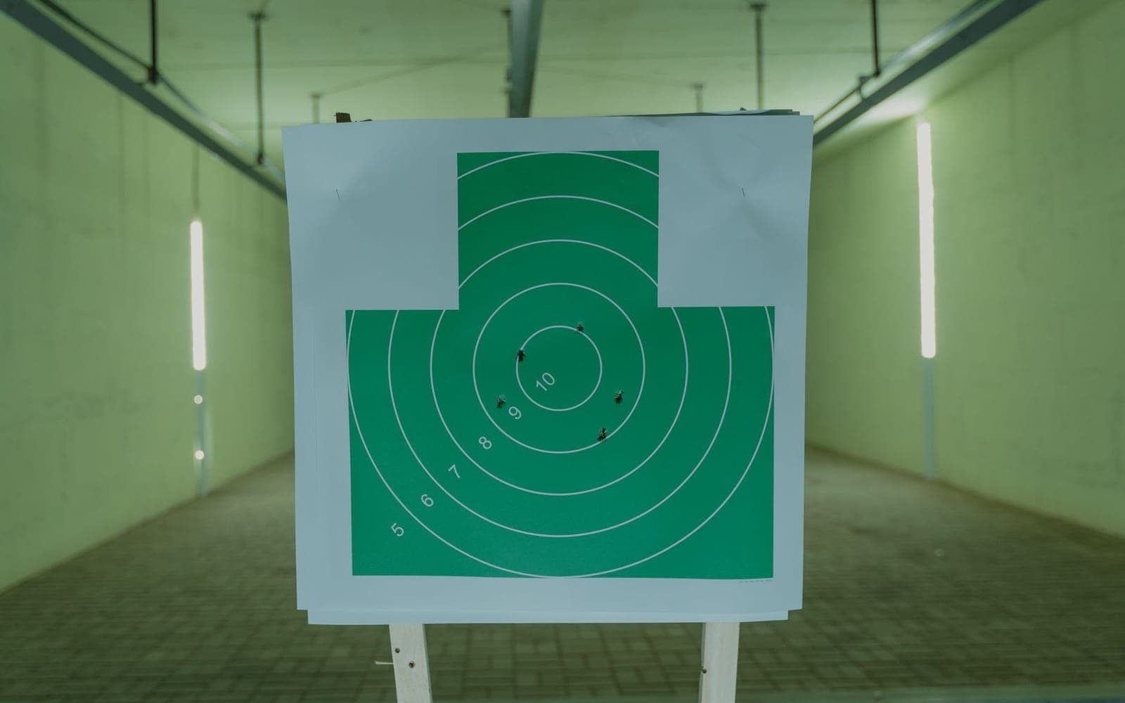 Illustrative stock photo: a green paper target with bullet holes hanging at an indoor range